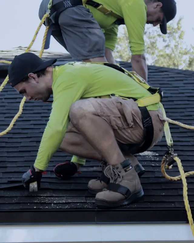 Two roofers in safety harnesses working on a roof