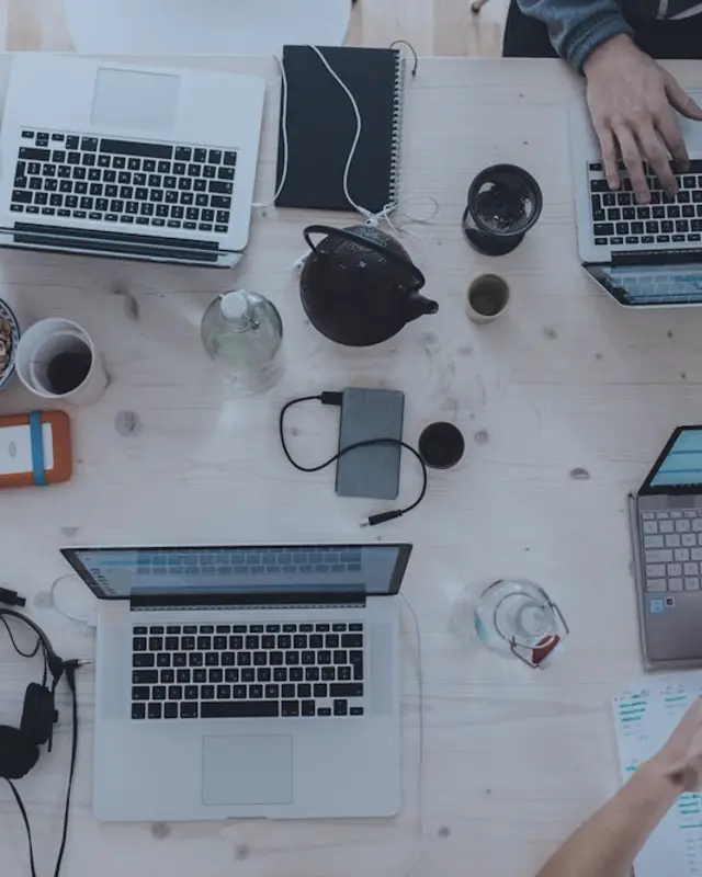 A team's laptops and phones on a shared desk, seen from above